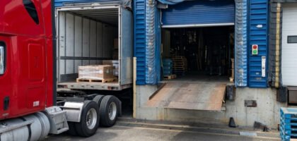 Camion semi-remorque rouge stationné à un quai de chargement d'entrepôt logistique avec nivellement hydraulique et porte sectionnelle