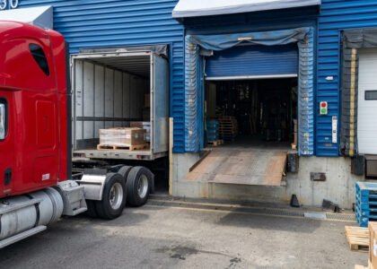 Camion semi-remorque rouge stationné à un quai de chargement d'entrepôt logistique avec nivellement hydraulique et porte sectionnelle