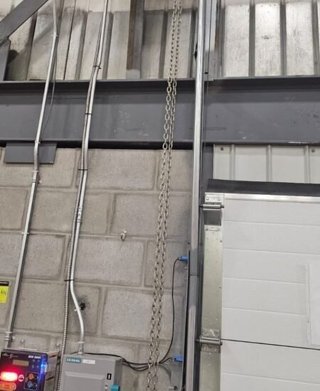 Moteur électrique à chaîne et panneau de contrôle installés sur une porte sectionnelle industrielle d'entrepôt